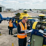 Helicopter safety inspection team examining rotorcraft turbine on airfield tarmac