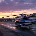 Sikorsky S-76 executive helicopter on airport ramp at sunset with purple and gold horizon