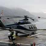 Sikorsky S-76 executive transport helicopter on helipad with misty coastal hills in background